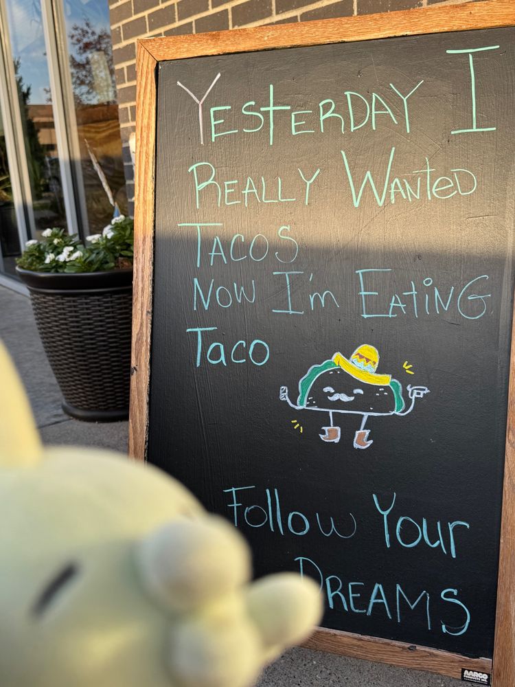 Gulpin in front of a sign. It says "Yesterday I really wanted tacos, now I'm eating taco. Follow your dreams."