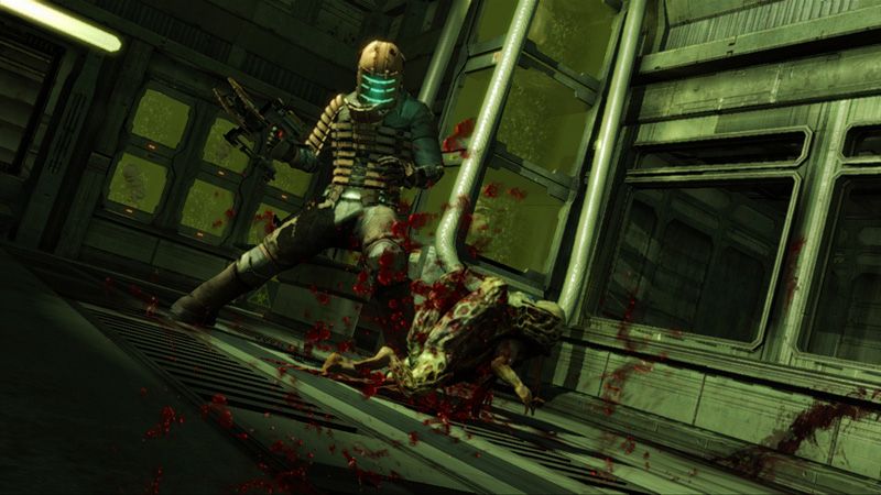 Screenshot from the video game Dead Space, depicting engineer protagonist Isaac Clarke stomping on one of the undead Necromorph creatures in a windowed room with sickly green lighting. Isaac is holding a futuristic power tool in his right hand.