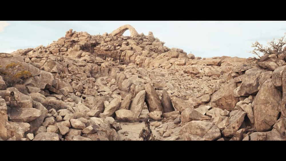 Wide establisher shot of Cold Rocks Hold, made up of hundreds of stacked large boulders. Our group of heroes walk through the bottom of frame towards Cold Rocks Hold in the distance. Camouflaged Aiel warriors hide amongst the rocks.