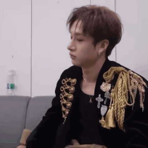 a man is sitting on a couch wearing a black jacket with gold embroidery and a necklace .