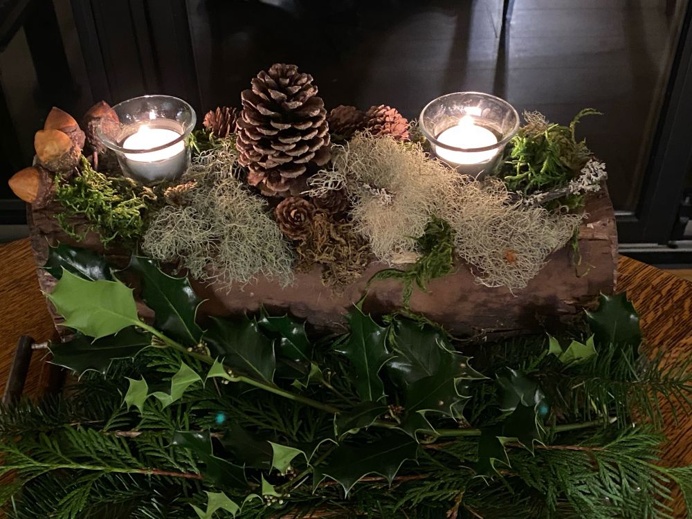 Photo shows a log with moss, pine cones, greens and 2 votive candles.