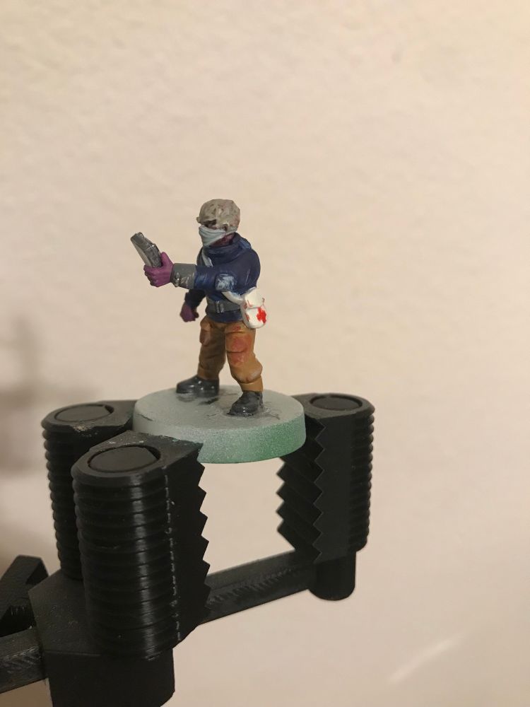 A miniature of an alien doctor holding a Star Trek tricorder-like device. The alien is wearing a medical mask and purple nitrile gloves. It has a blue jacket on and tan pants, which are stained with dried blood. The alien’s skin is a mottled gray.

Visible from this angle is that the alien has a white medical bag with a Red Cross on it, also lightly stained with dried blood.