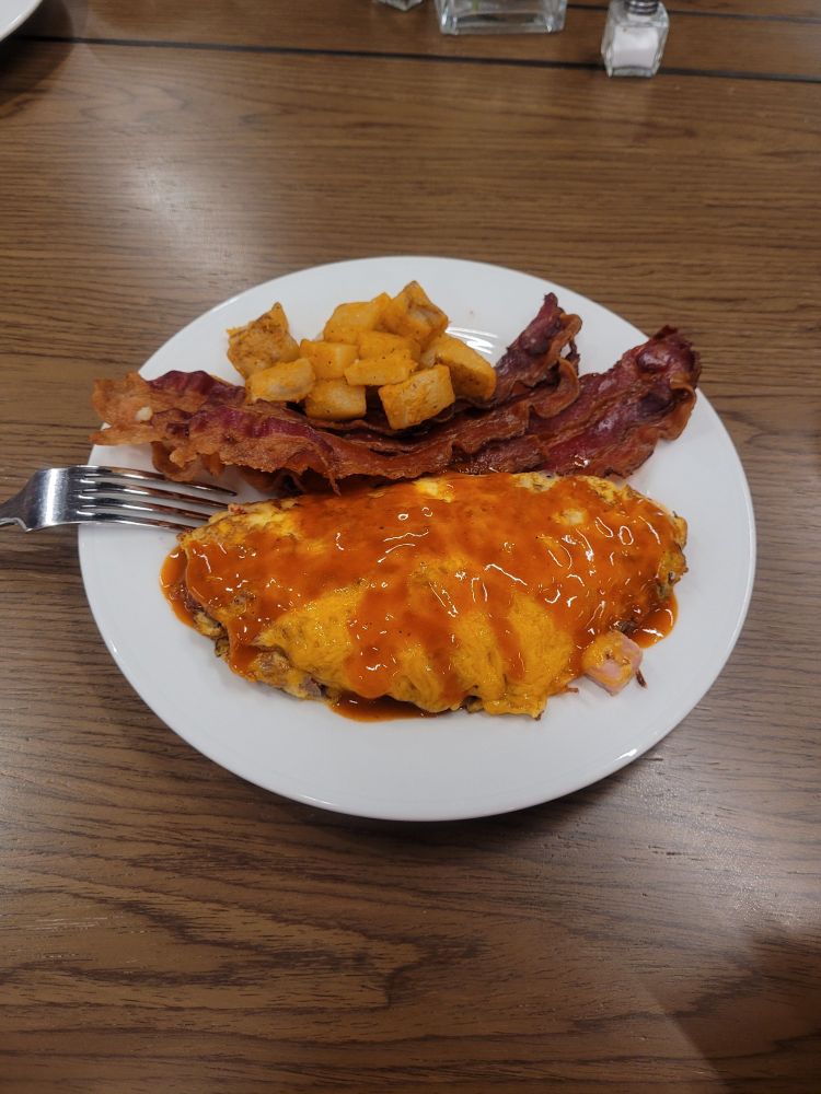 Plate with omlette covered in sauce, bacon, and potatos