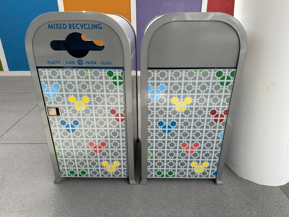 Silver trash cans featuring a line and circle patterns on the side, with select colored circles creating Mickey heads in the pattern, located at Disneyland