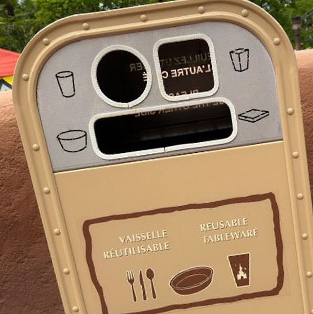 A trash receptacle with multiple slots for disposal, featuring icons for cups, food containers, and reusable tableware. Text is in both English and French, indicating proper disposal methods.