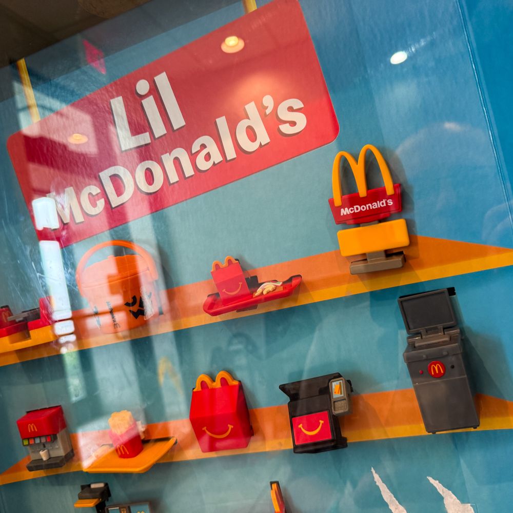 A colorful display titled "Lil McDonald's" featuring miniature McDonald's food items and restaurant accessories, including a Happy Meal, fries, and a cash register.