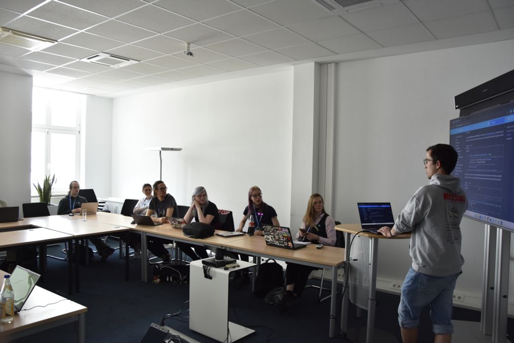 A group of people in a conference room, listening to the speaker and trying things out on their laptop.