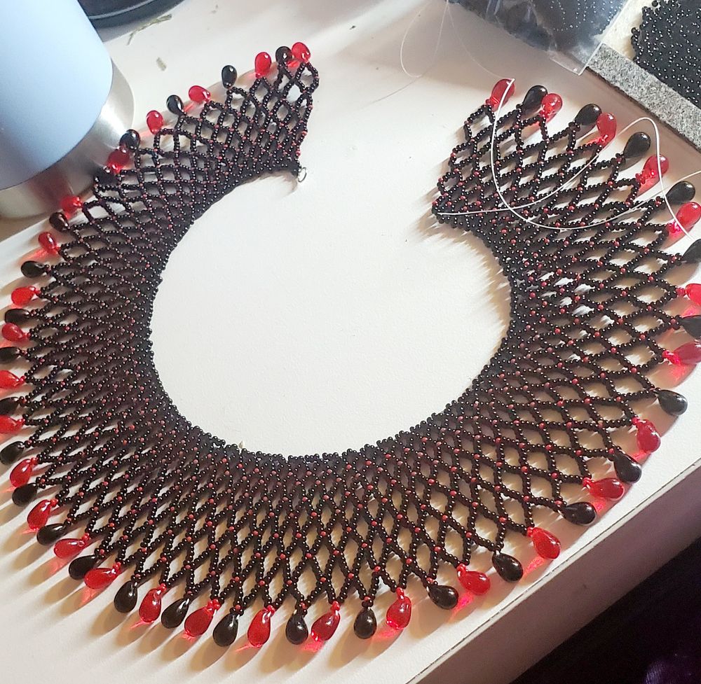 Beaded choker in progress with black and red seed beads and glass teardrops.
