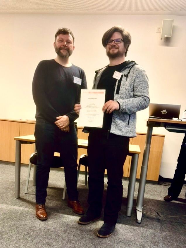 Johannes Ebner (rechts) hält die von Tobias Boll (links) überreichte Urkunde des Christel Hopf-Preises in die Kamera.