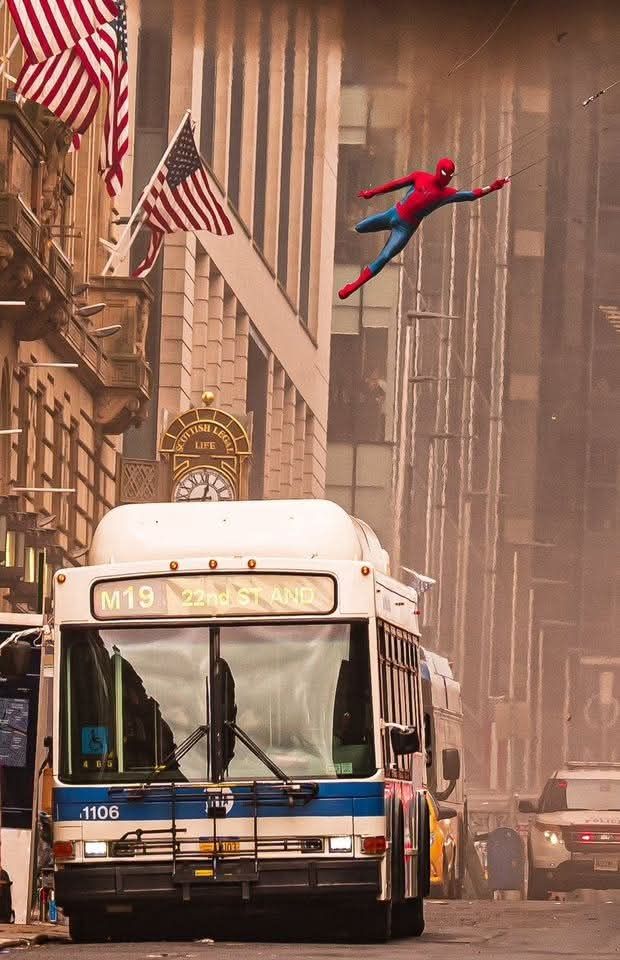 A Glasgow street dressed up as New York with American vehicles and flags, through which your actual Spider-man appears to be swinging.