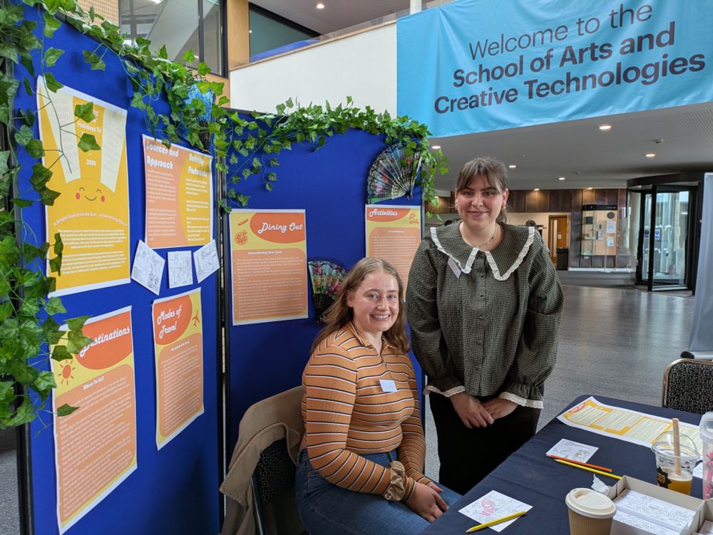Zuzanna Róg and a colleague at the stand. There are colourful posters behind them and a table in front of them with different activity cards