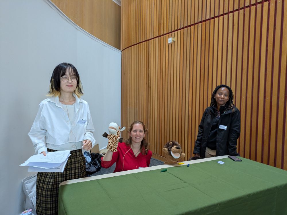 The team: two humans, one human with a giraffe puppet and then one puppet (a lion) at their exhibition stand.