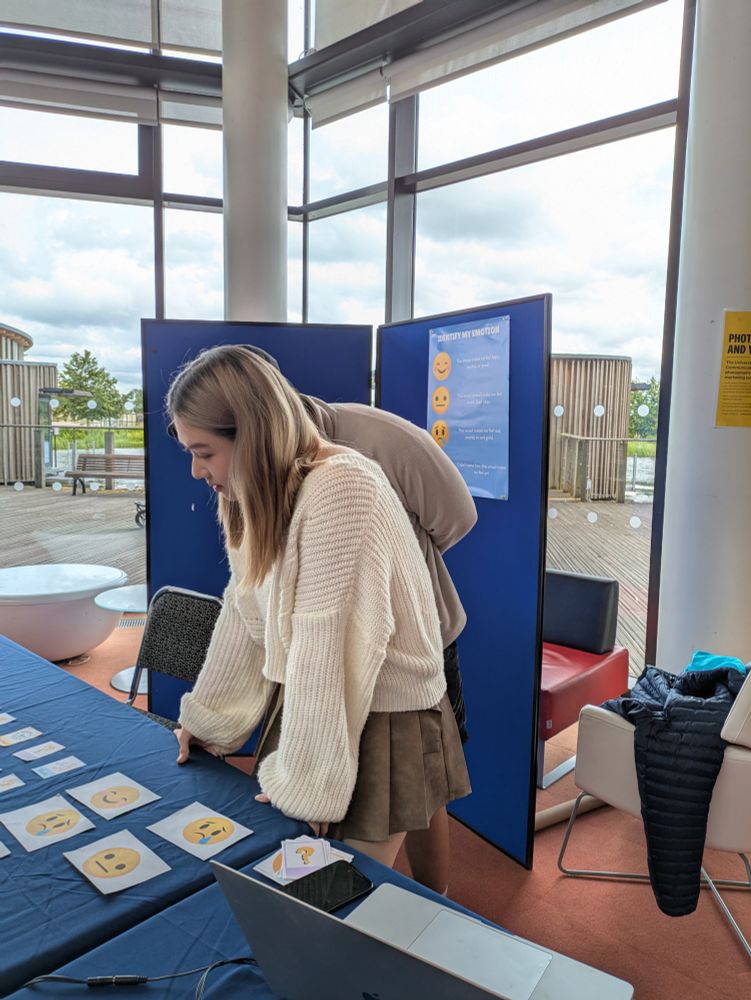 Sylvia at her exhibition stand. There are cards with different emojis, including smiling, sad and neutral faces. 