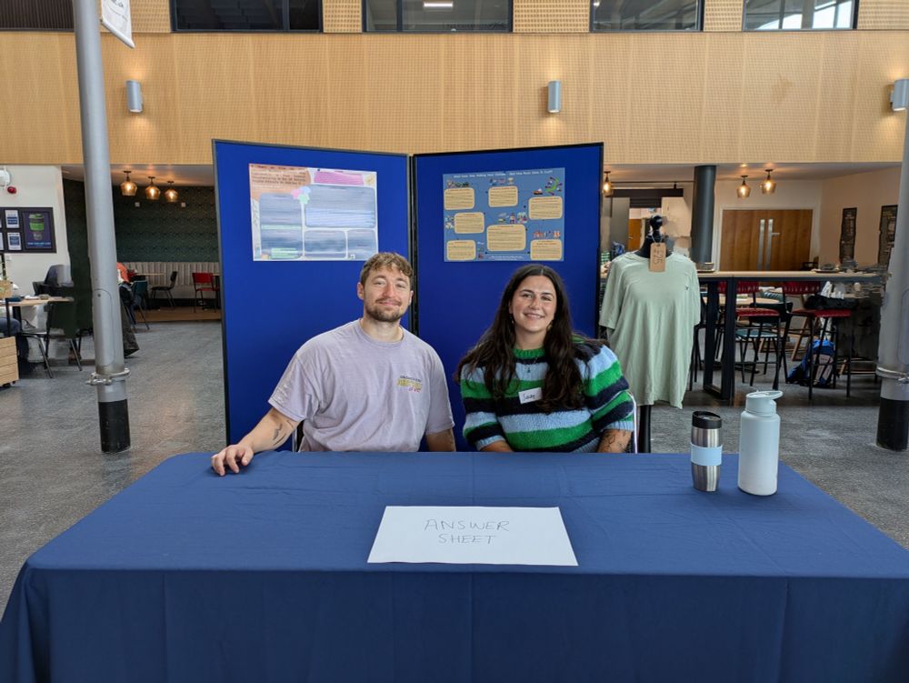 Susy Williams and another presenter at their exhibition stand. There is a piece of paper on a table that says 'Answer Sheet' 