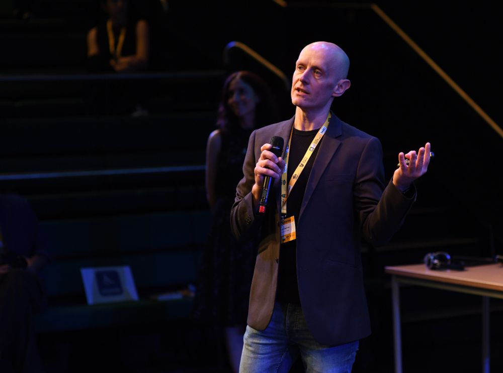 Photo of Gavin Kearney presenting, holding a microphone and a clicker