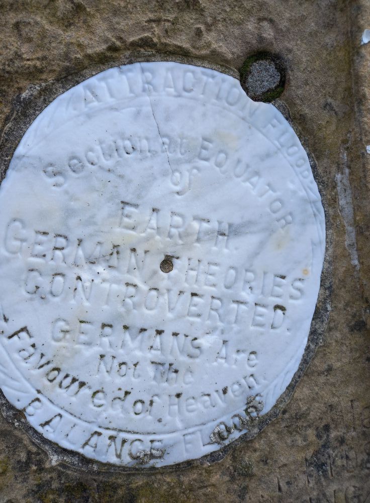 An engraved inscription that reads:

This diagram illustrates the cause of the so called Earth Tides. Also each alternate Ocean Flood, the cause of which has never yet been understood.

RE EARTH TIDES: we are told that the Moon raises the solid surface of the Earth under it about 8 inches and raises the OPPOSITE SIDE 8. This I hold to be impossible. The phenomenon called EARTH TIDE IS CAUSED BY E-H’s WEIGHT PULLING …

[The remainder of this stone has worn but the Geograph contributor was informed that it ended: AGAINST THE SUN’S ATTRACTION.]

The water flows back when att’n over & forms a heap on opposite side of E. to balance att’n flood. There is no … 
