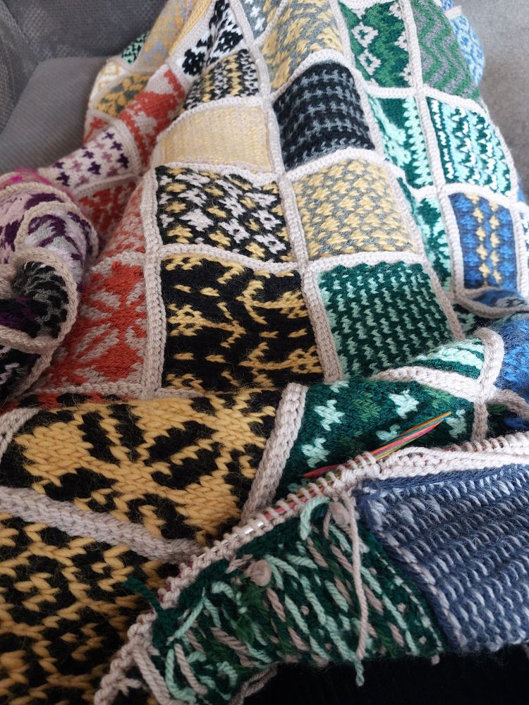 The Peace By Piece blanket designed by Needle and Feather with the border on knitting needles 