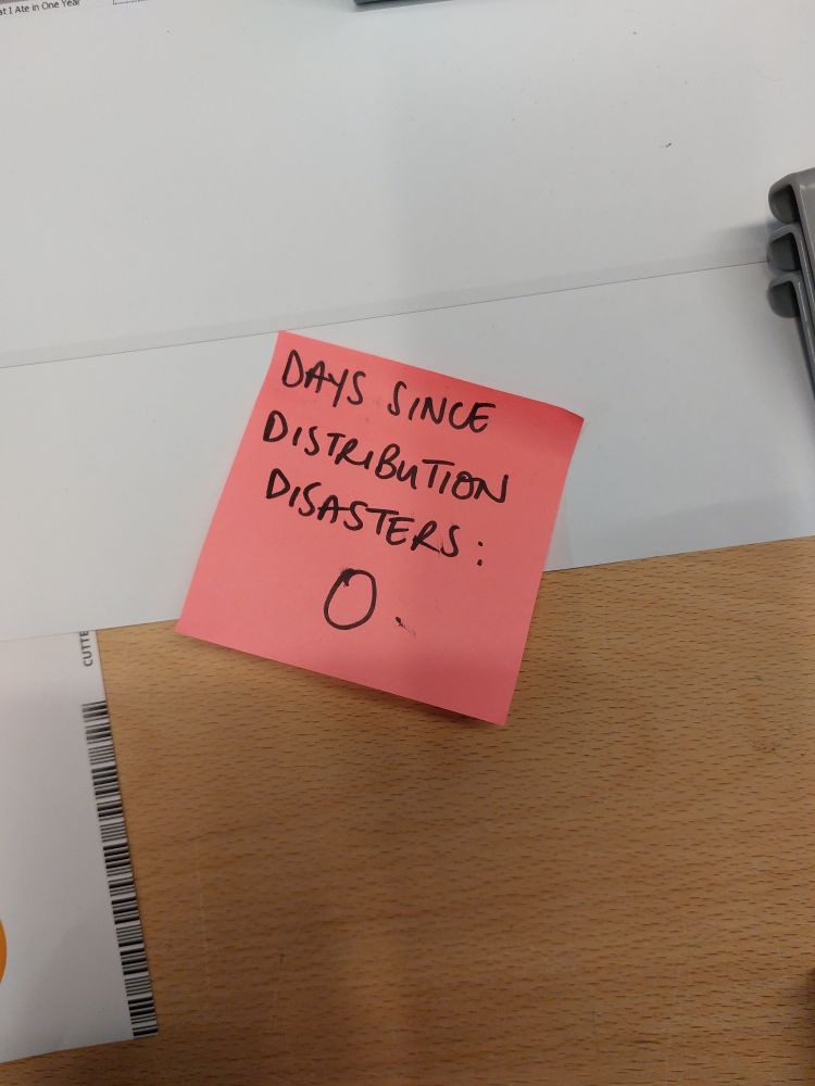 A pink post note on the desk saying "days since distribution disasters: 0"