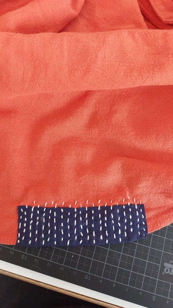 A coral shirt with a navy blue patch, attached with running stitches in unbleached cotton yarn