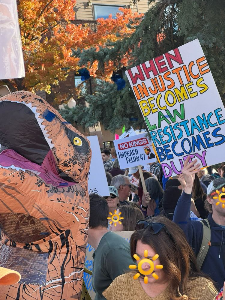 Close up of crowd of protesters with signs and an inflatable T-Rex costume 