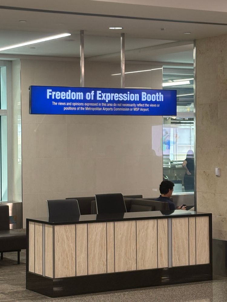 An empty table with two seats and a sign that says ‘Freedom of Expression Booth’. An air of sadness pervades