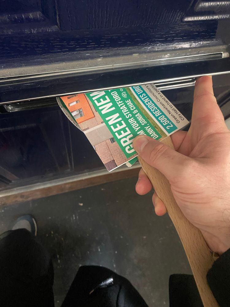 Man inserting a Newham Green Party leaflet through a letterbox with the use of a spatula.