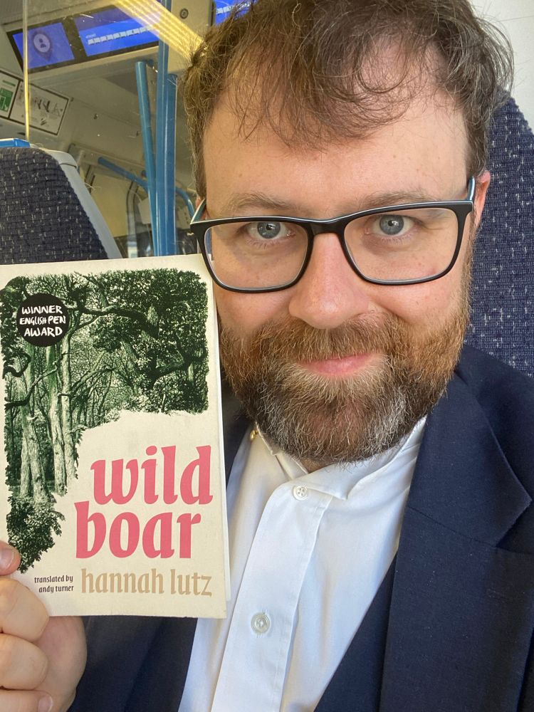 Man holding a copy of ‘Wild Boar’ by Hannah Lutz