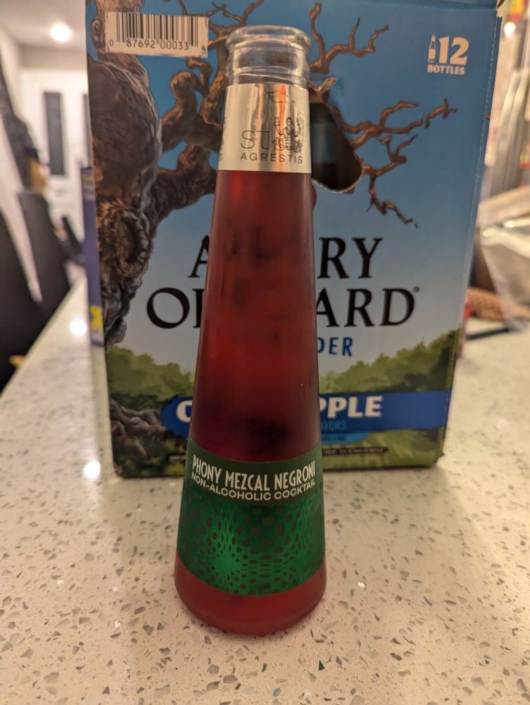 A glass bottle that says "phony mezcal negroni" on it. The liquid in it is red and the label is green.