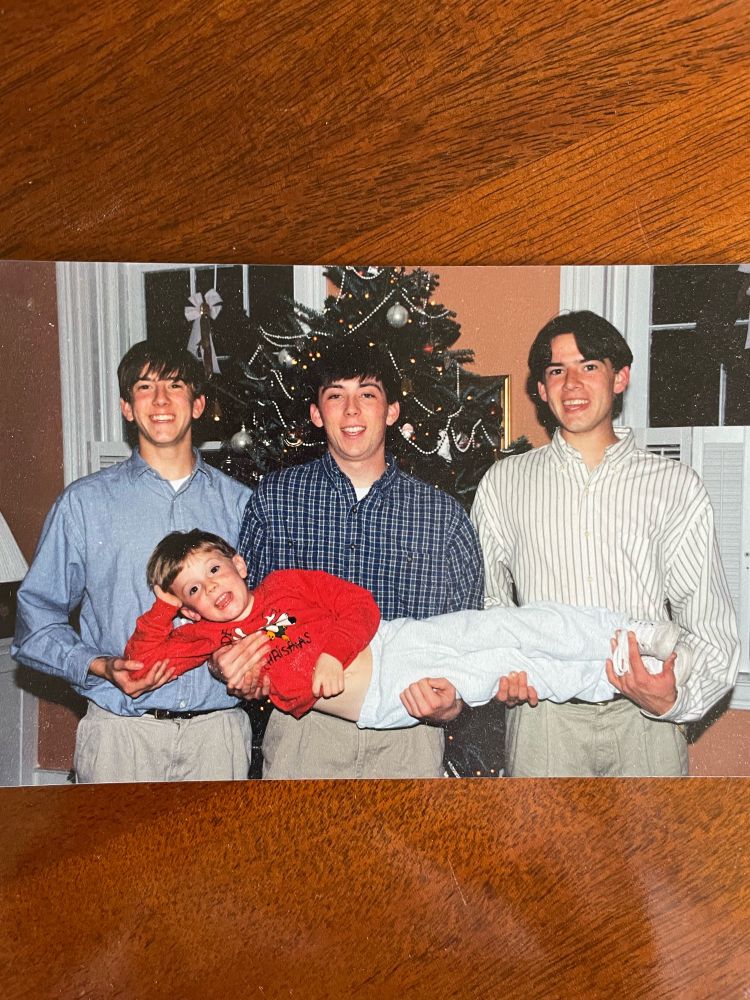 Christmas picture from the 90s. Three older brothers are holding up the youngest, more charming brother