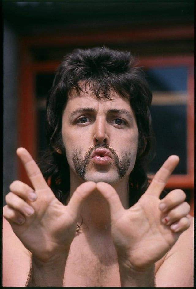 Paul McCartney, rocking a sick mullet and flared handlebar, puts up a W with his fingers. 