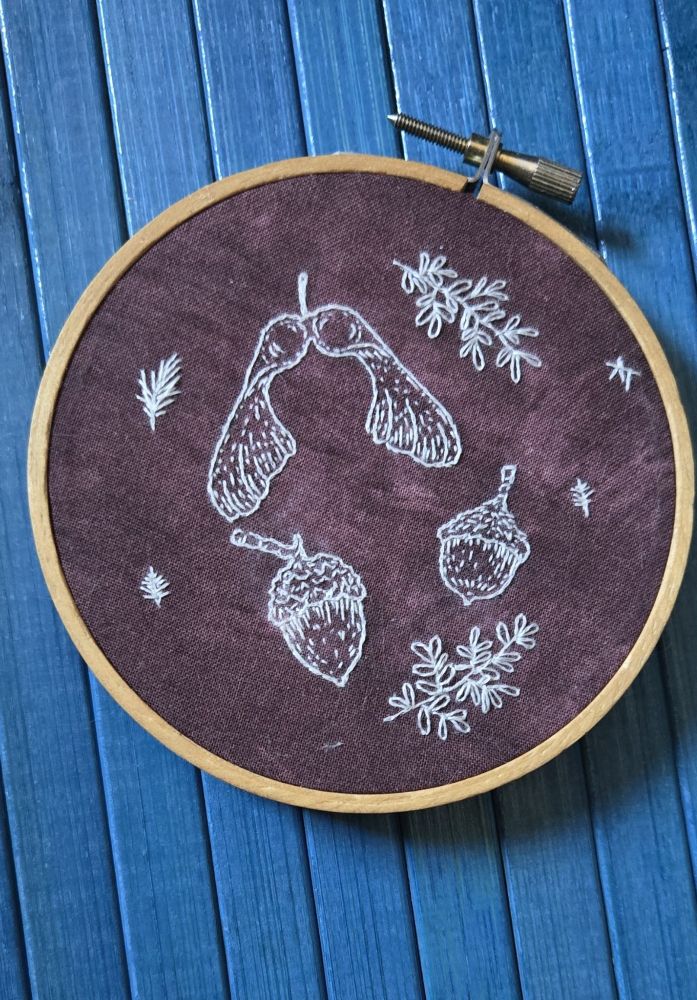 Embroidered acrorns and maple seeds on a burgundy fabric. 