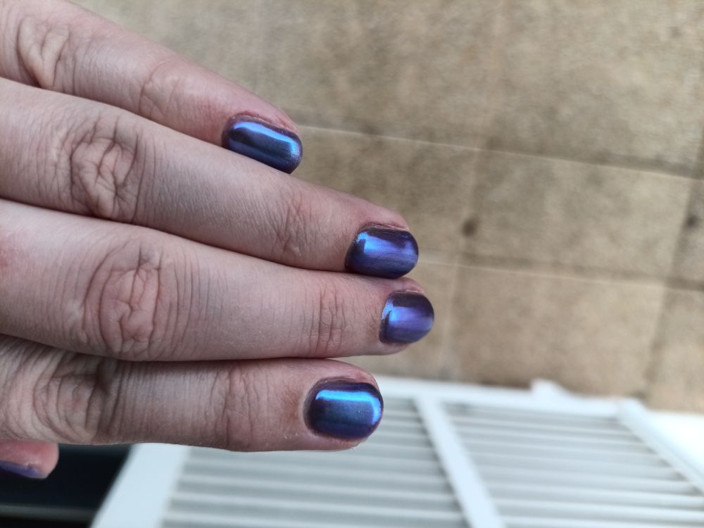 Left hand finger with nail polish. Each finger is angled in slightly different way to show the different shades. The color goes from a light aubergine to lilac with some lighter blue highlights. There is a slight aurora shine and sparkle across the nail.