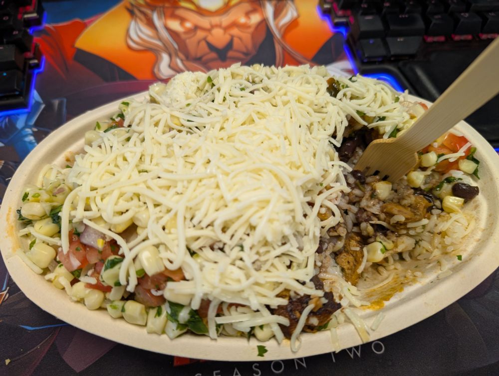 An overfull burrito bowl from Chipotle on a desk with a Dice Throne playmat.