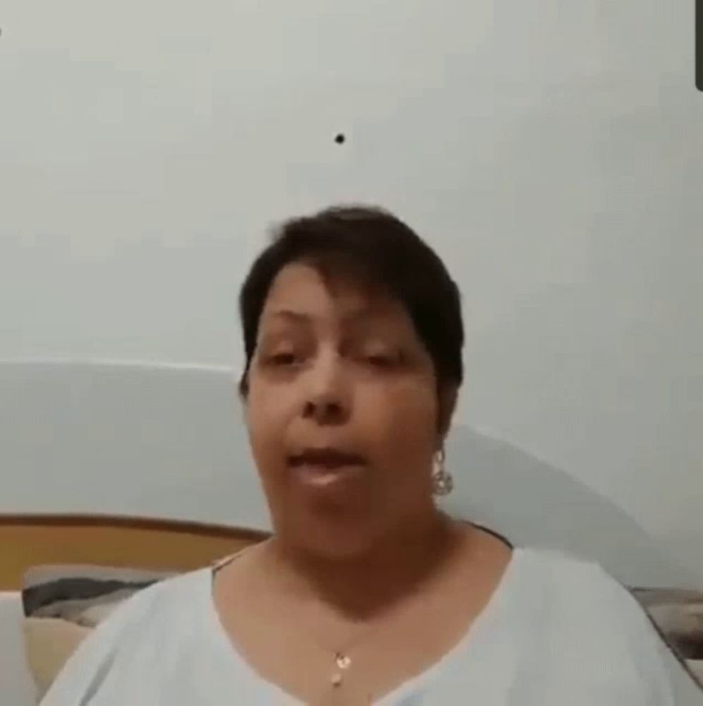 a woman in a white shirt is making a funny face while talking on a video call .