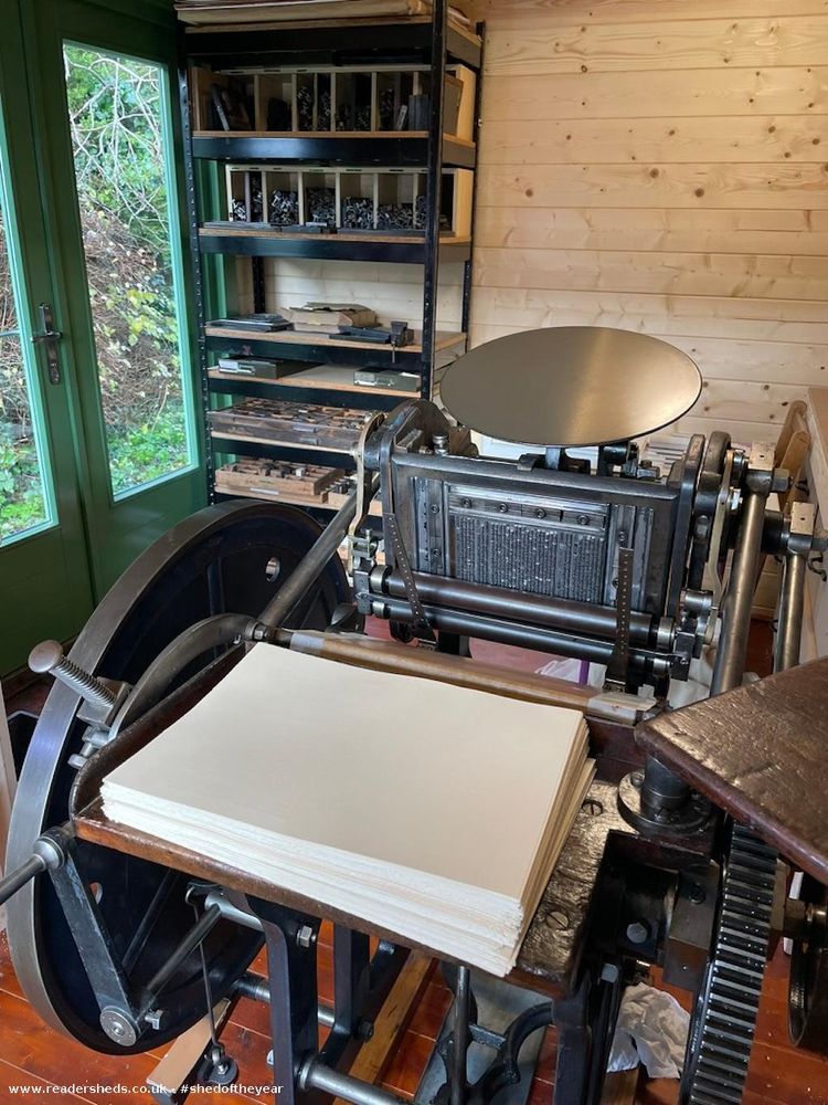Focuses on the printing press with a stack of blank paper ready to be printed. The intricate mechanics of the press are visible.