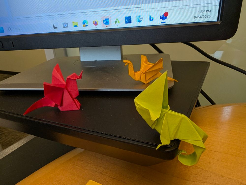 Another monitor stand, with two origami dragons in a standoff, being watched by a large oversized origami chameleon.