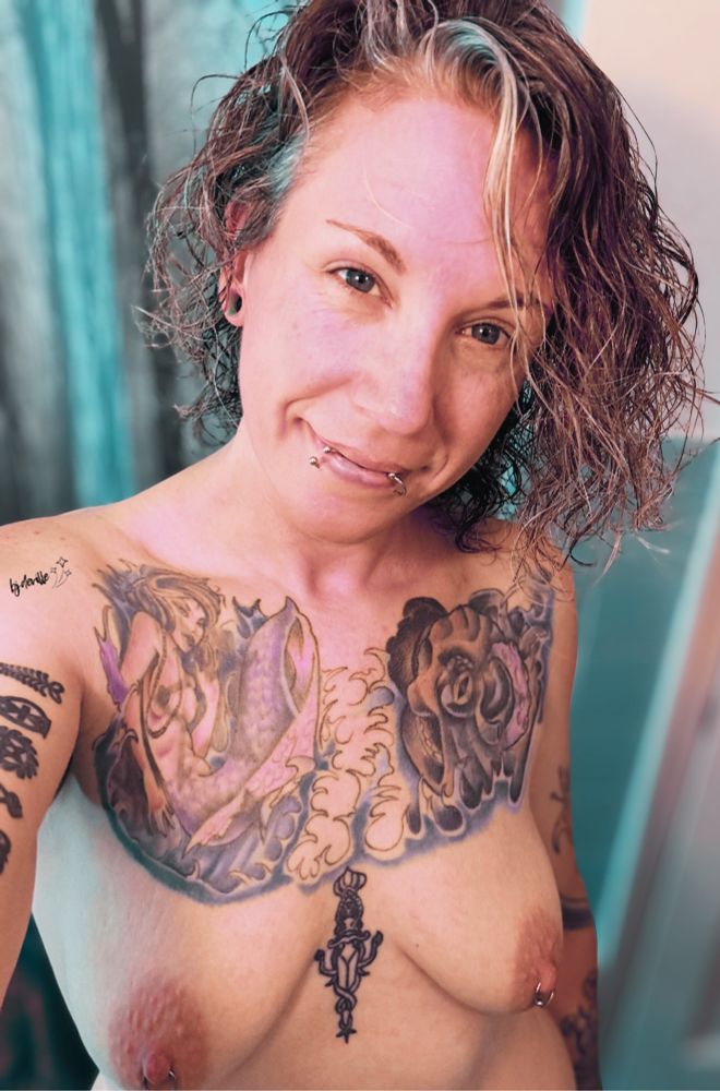 An alternative MILF stands naked exposing various tattoos and small pierced breasts. 