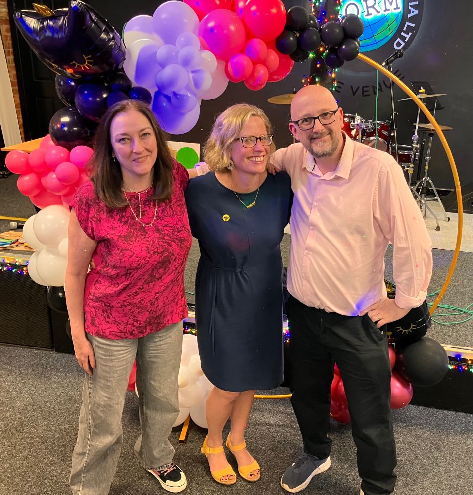Rob, Hannah and Elaine smiling in front of balloons