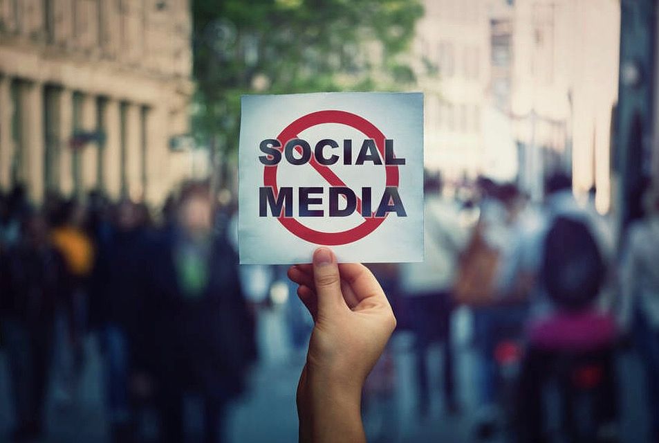 Someone holding a sign that has the words Social Media crossed out. 