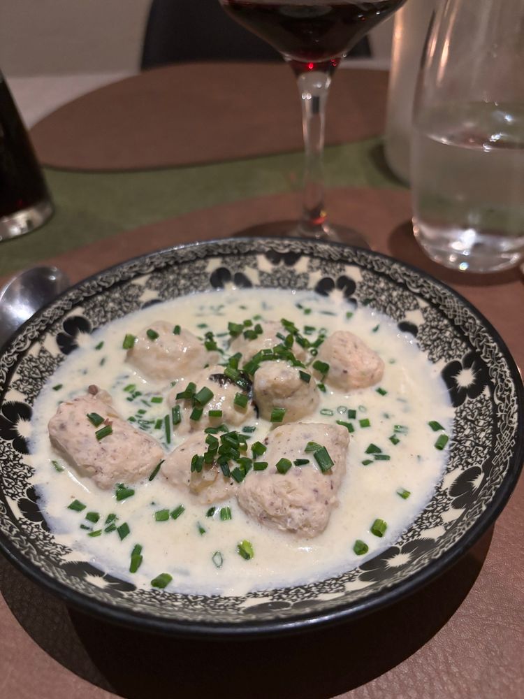 Eine Vorspeisw auf einem Teller mit schwarz weißem Blütendekor:
Weiße Knoblauch Soße, darin Fischstücke und Kräuter drauf