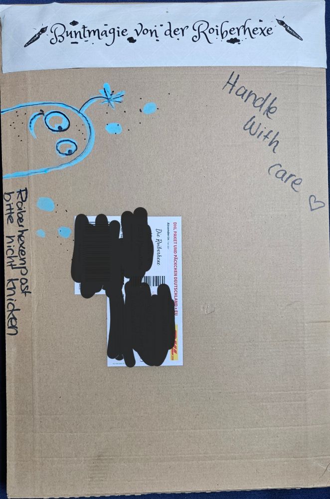 Ein hellbrauner Paketumschlag mit aufgehalten blauen bubblegeist, Text "Roiberhexenpost bitte nicht knicken und einem weissen Aufkleber mit dem Text Buntmagie von der Roiberhexe