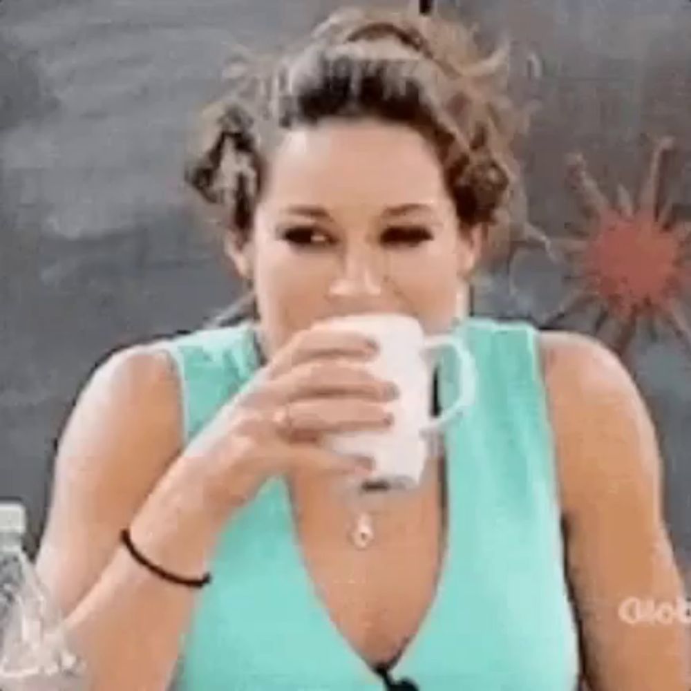 a woman in a blue shirt is drinking from a white cup .