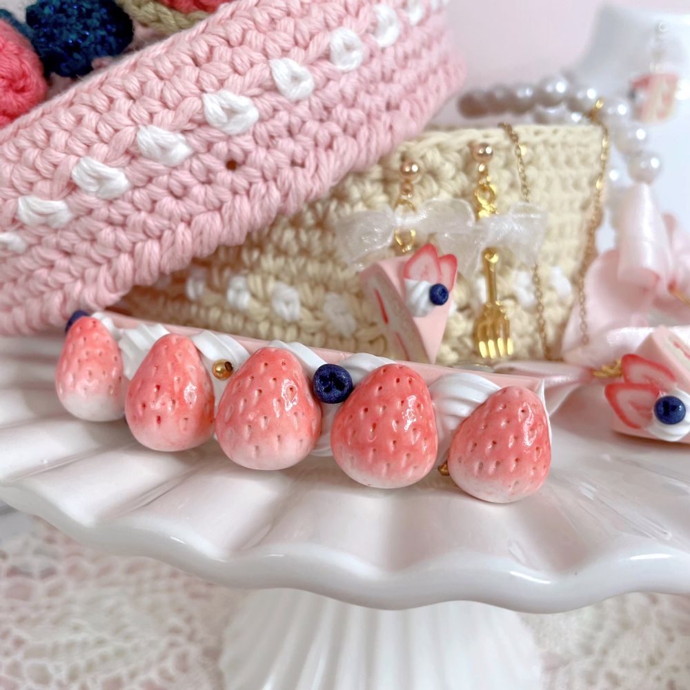 A close up of a hair clip with clay frosting, blueberries, and strawberries on top.