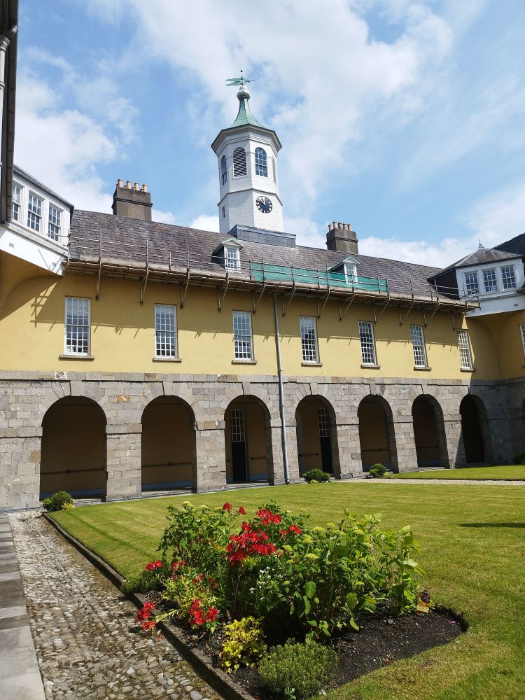 Covered walkway with a second story and wooden cupola that has a clock and weather vein