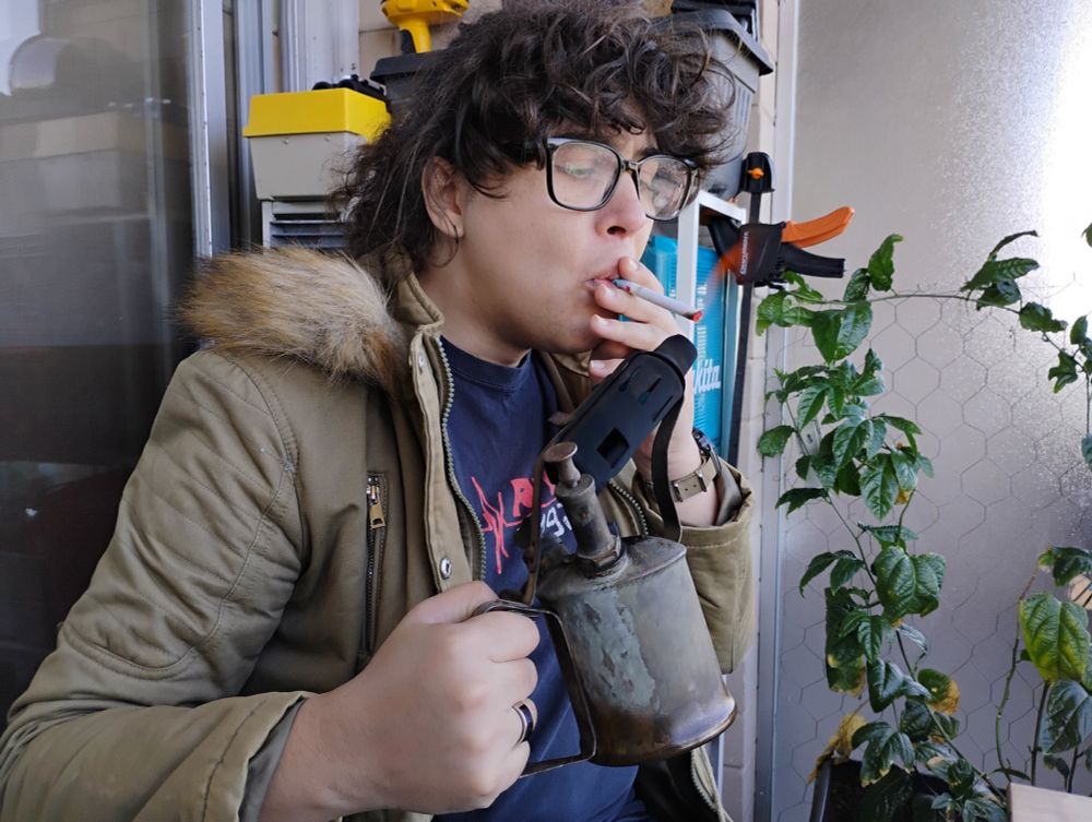 Allison lighting a cigarette with a grimy old kerosene blowtorch