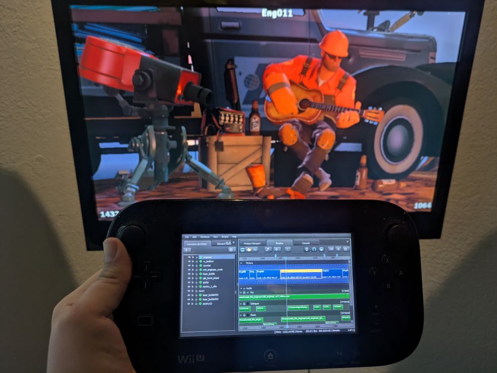 Photo of a Wii U Gamepad controller being held with a television in the background. The Gamepad display shows the user interface for Source Filmmaker with a timeline view. The television shows the viewport with character animation.
