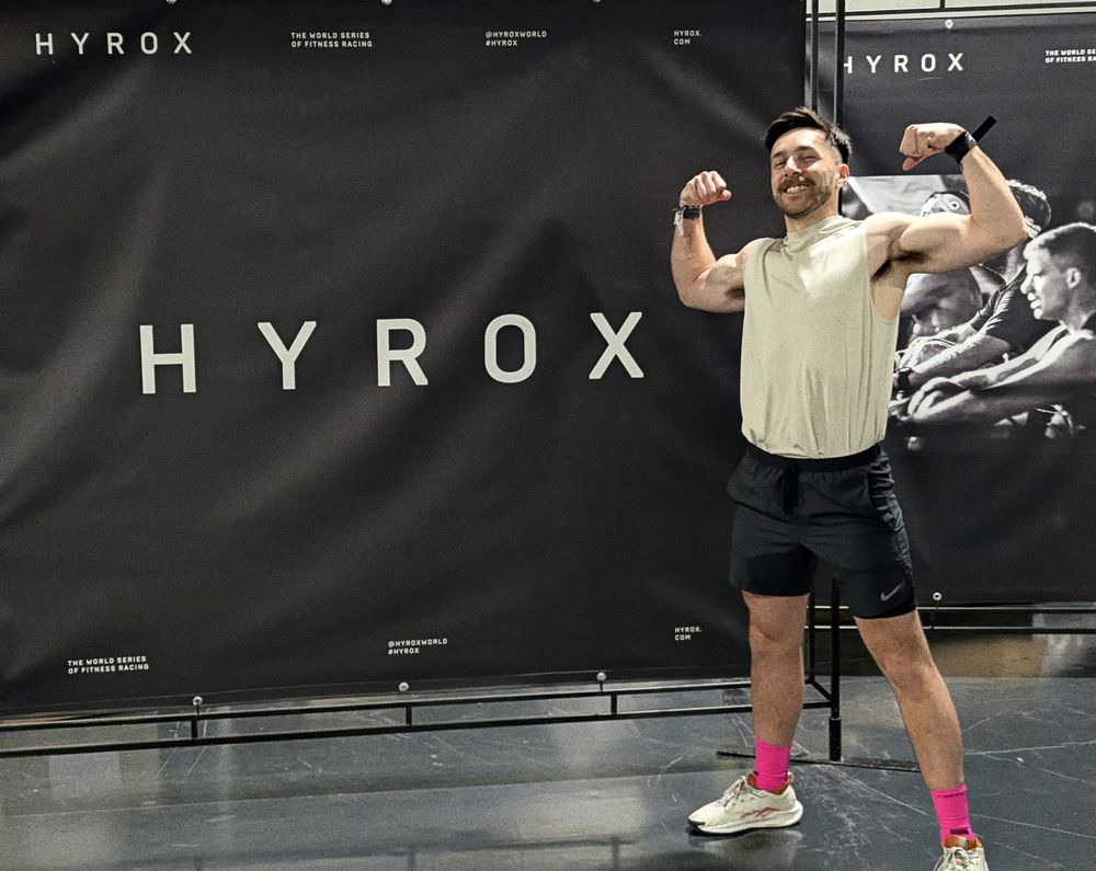 me posing in front of a large "HYROX" banner in gym wear
