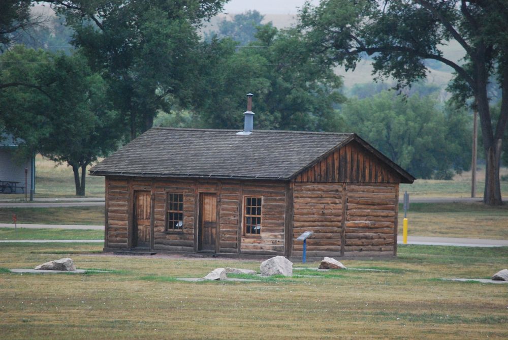 An old, small, brown wooden building with trees in the background.
