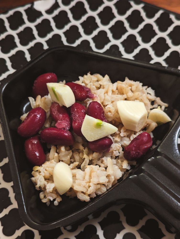 Ein Raclette-Pfännchen mit Vollkorn-Basmati-Reis, Kidney-Bohnen und einigen Stücken Knoblauch.