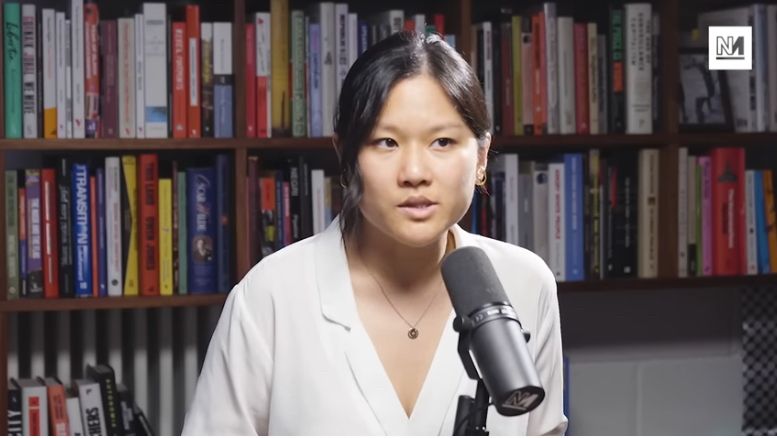 Close up of journalist Karen Hao speaking into a mic with a background of bookshelves. 